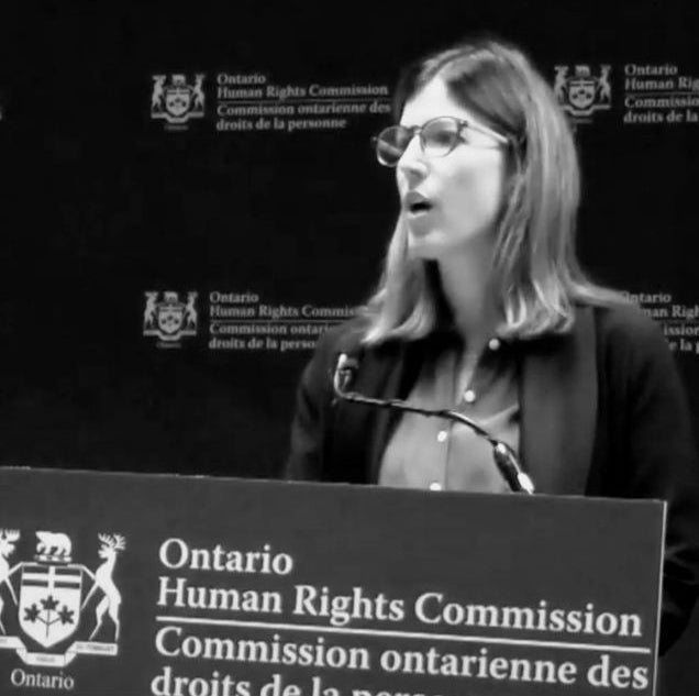 Lark Barker speaking at the podium for the Ontario Human Rights Commission Right to Read Inquiry.
