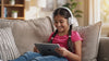 Smiling young girl with headphones having fun using Lexia on a tablet, representing advanced reading enrichment and decoding with the Radical Reading SURGE Program.