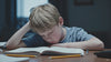 Grade 3 or 4 boy struggling to read a book looking miserable illustrating a child who needs the Radical Reading REWIRE Program.